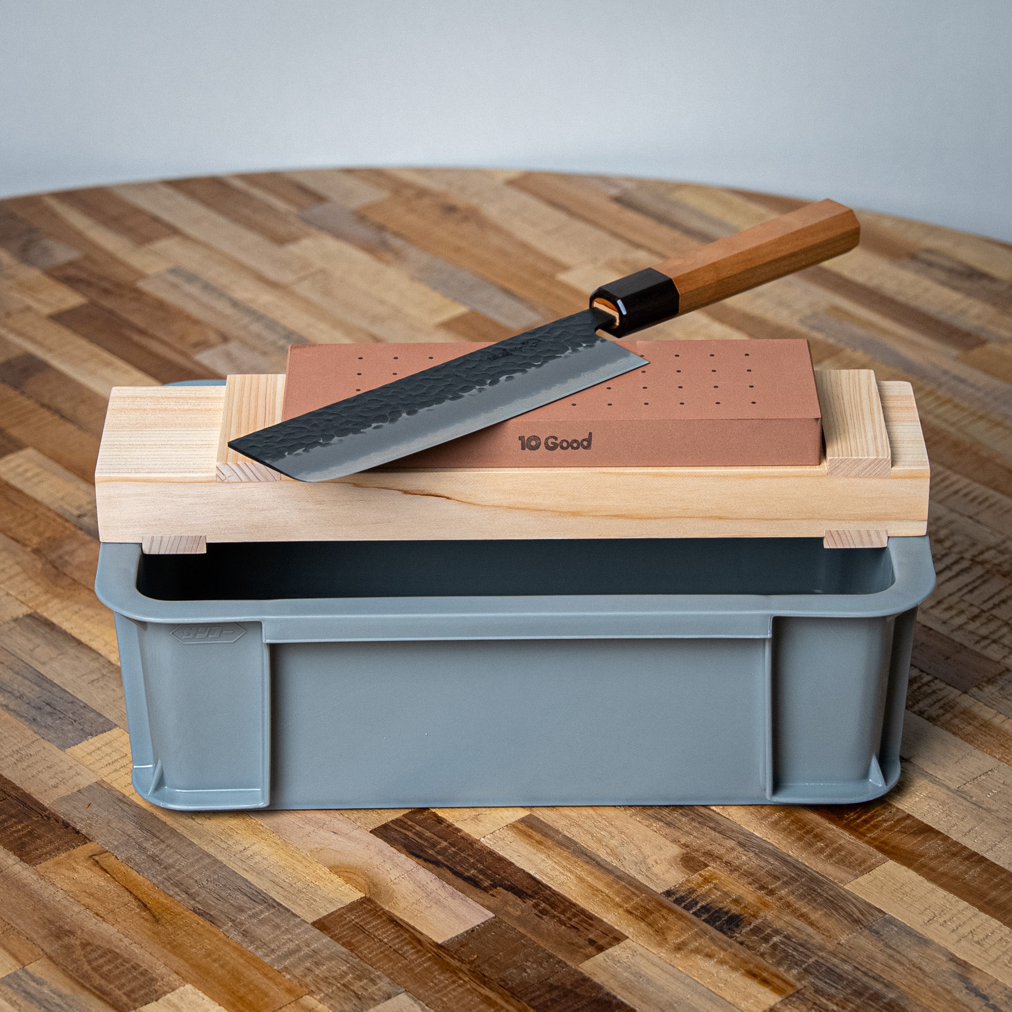 Couteau japonais sur pierre 10Good, manche en bois clair et ferrule foncée visibles.

