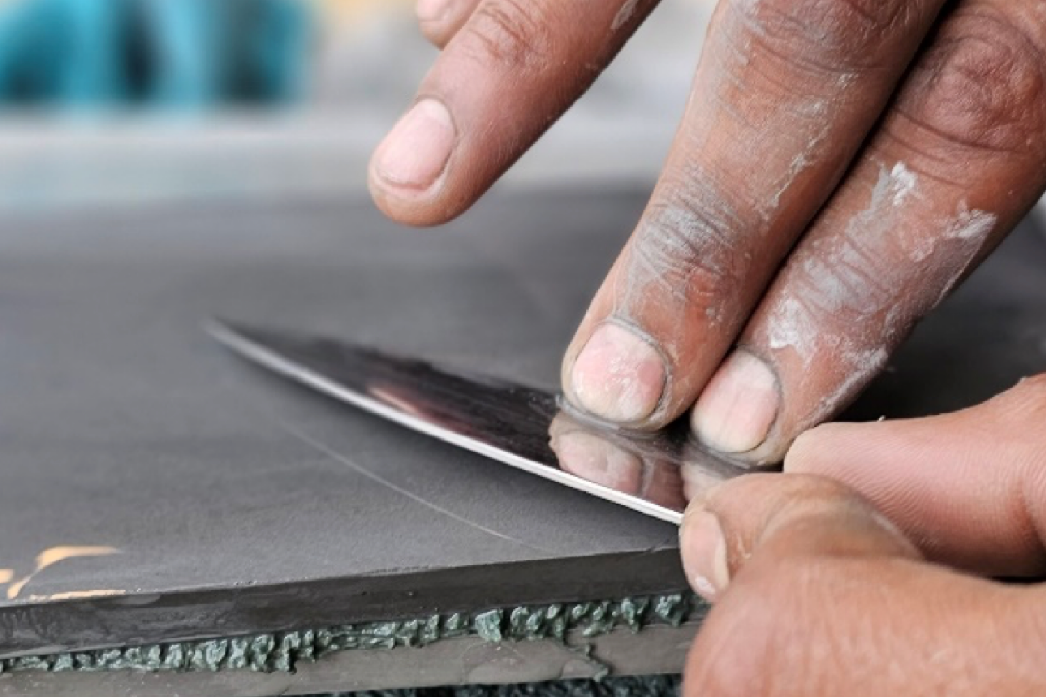 Man's hands sharpening a knife blade on a whetstone, showing precise angle and technique.