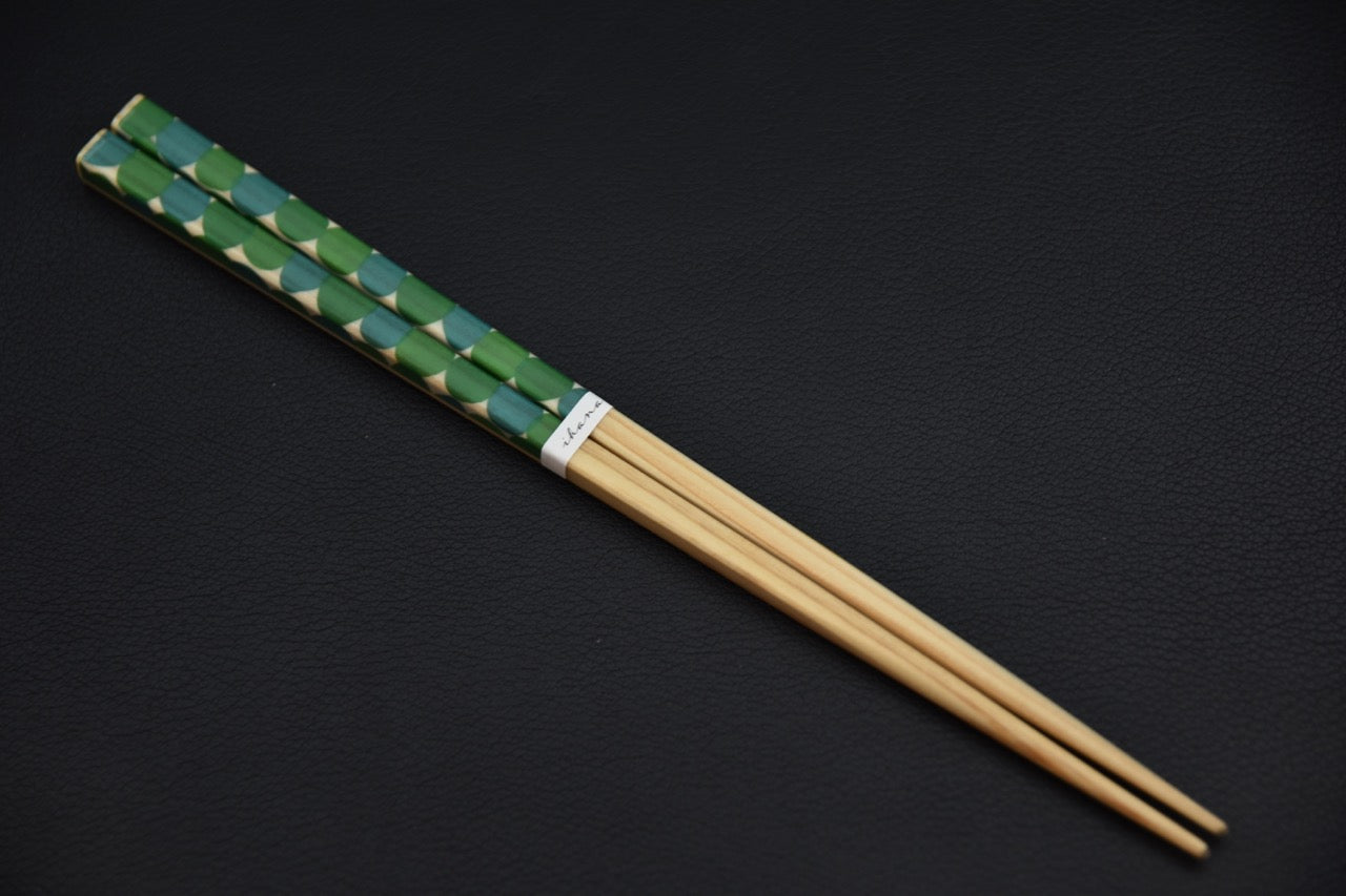A pair of Japanese chopsticks ‘Ihana Saison – Green Dots’ displayed on a dark background, lacquered wooden chopsticks with green polka-dot motifs.