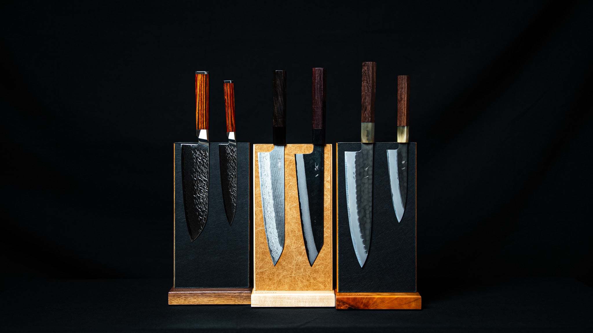 Couteaux japonais alignés sur supports magnétiques Stay Sharp en bois massif, vue de face sur fond noir, présentation complète.