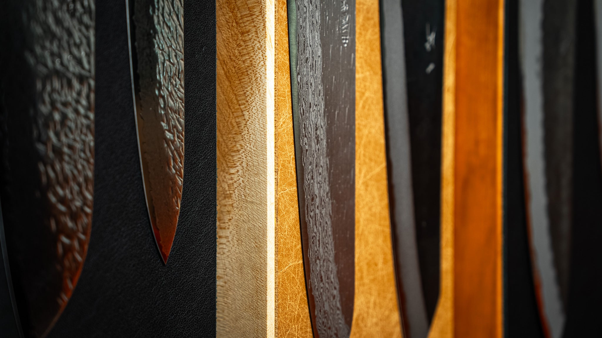Détail rapproché de couteaux japonais Gyuto exposés sur des supports magnétiques en bois massif noir, érable et merisier, finition cuir.
