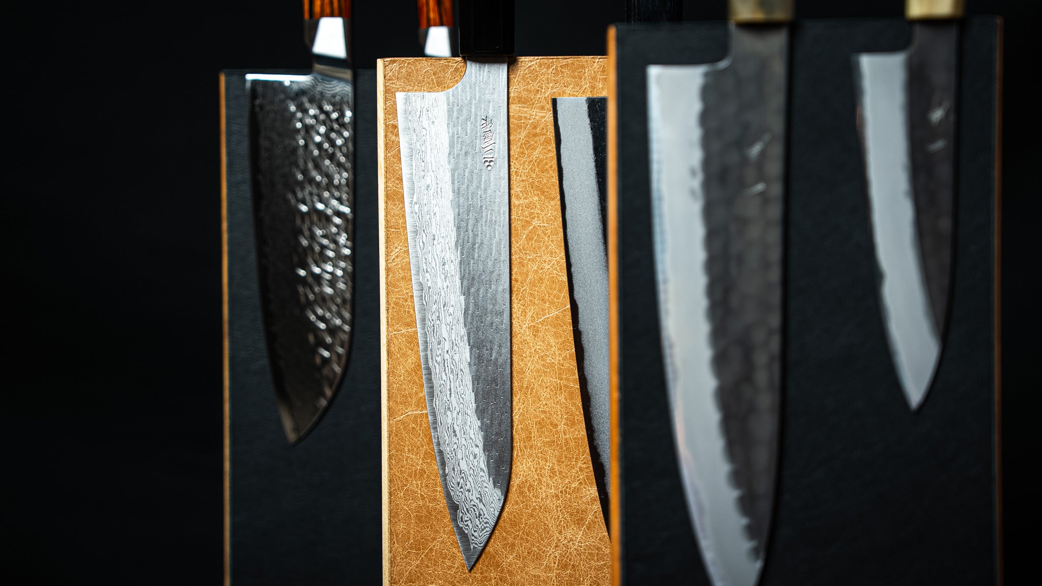 Couteaux japonais sur support magnétique vertical en bois et cuir brun clair, artisanat local Stay Sharp, photo centrée sur la lame.