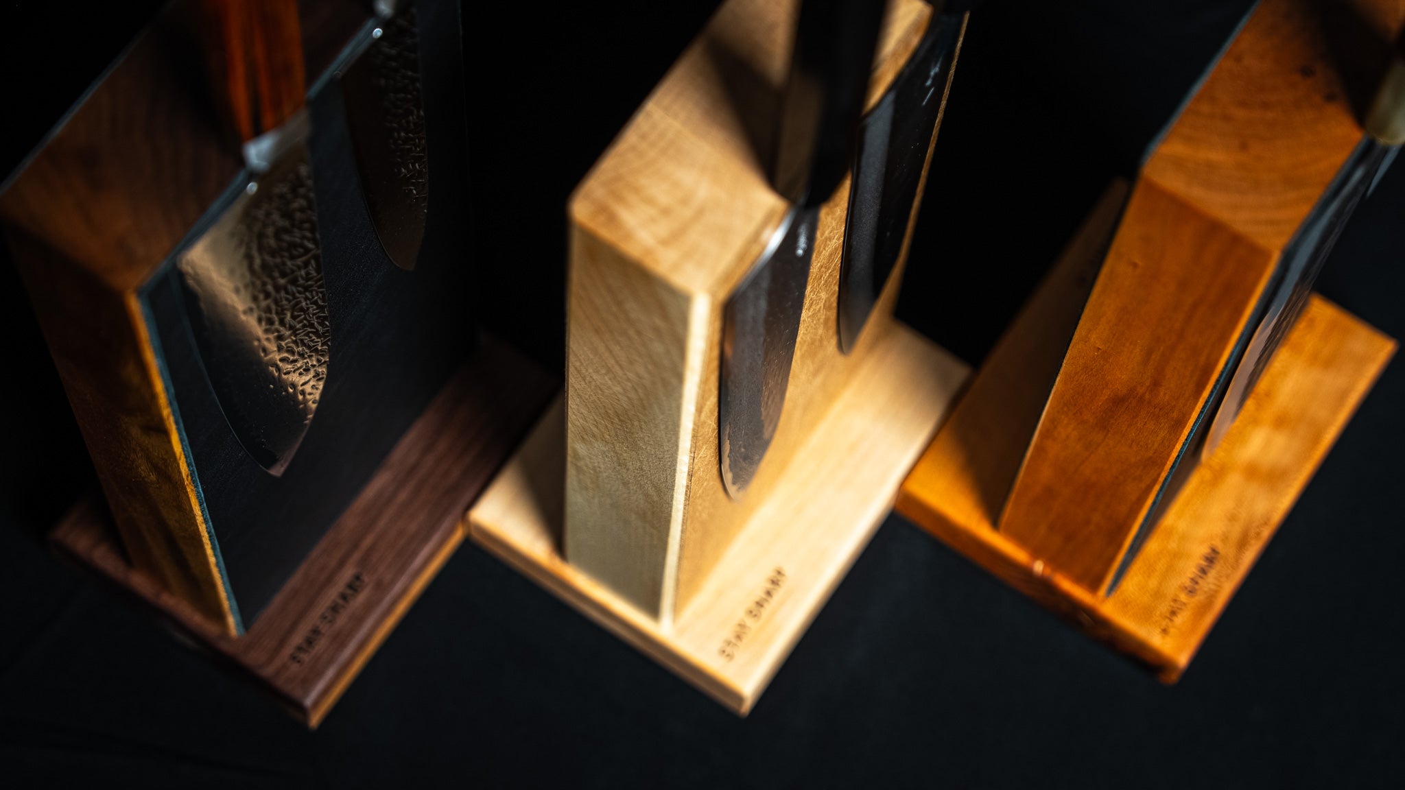 Vue plongeante de trois supports magnétiques pour couteaux de cuisine, en bois d’érable, noyer et merisier, avec gravure Stay Sharp.