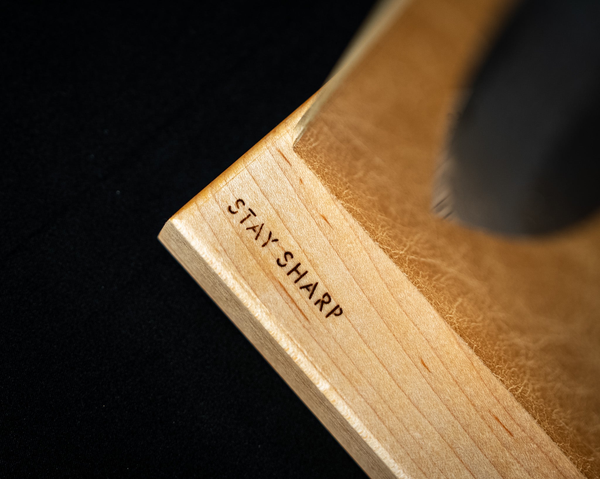 Gros plan sur la base en érable d’un support magnétique pour couteaux japonais, avec gravure Stay Sharp et surface en cuir brun.
