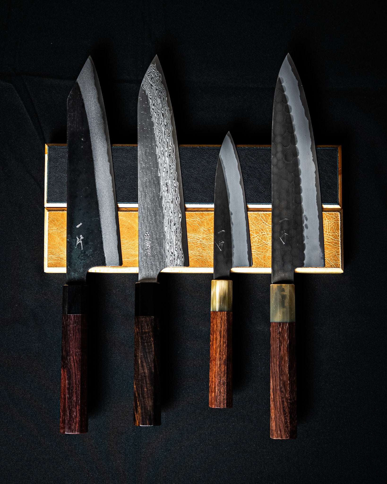 Support mural magnétique en bois clair avec cuir brun et noir, présenté avec quatre couteaux japonais à lame damassée.