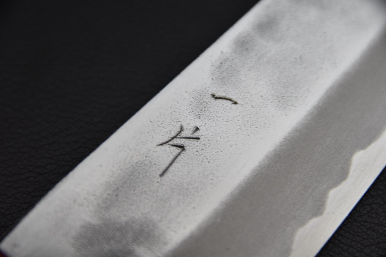 Couteau japonais santoku — gros plan sur la finition tsuchime et les kanji gravés sur la lame