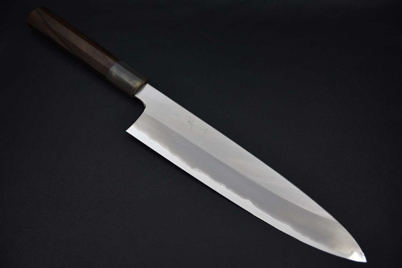 Japanese chef knife with a polished long blade and dark wooden handle, displayed on a black background.