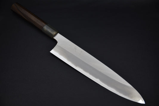 Japanese chef knife with a polished long blade and dark wooden handle, displayed on a black background.