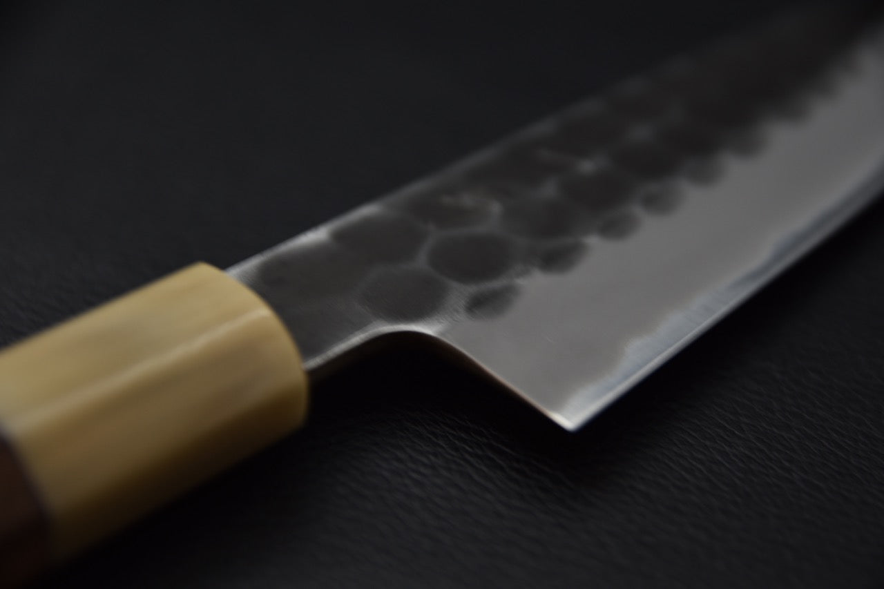 Gros plan sur un couteau japonais Petty avec lame martelée et manche en bois sur fond noir