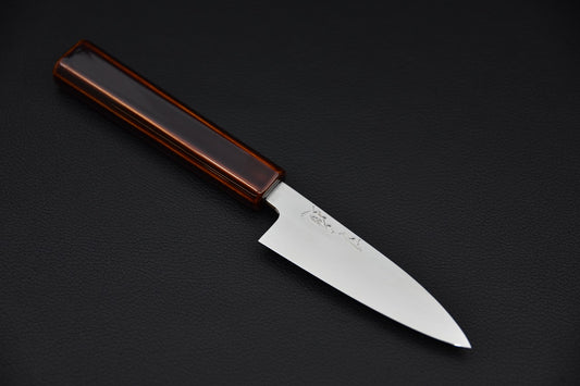 Japanese paring knife with a polished stainless steel blade and a lacquered wooden handle, displayed on a black surface.