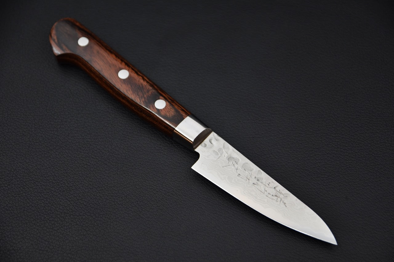Japanese paring knife with a polished blade and a dark imitation mahogany handle featuring three rivets, displayed on a black surface.