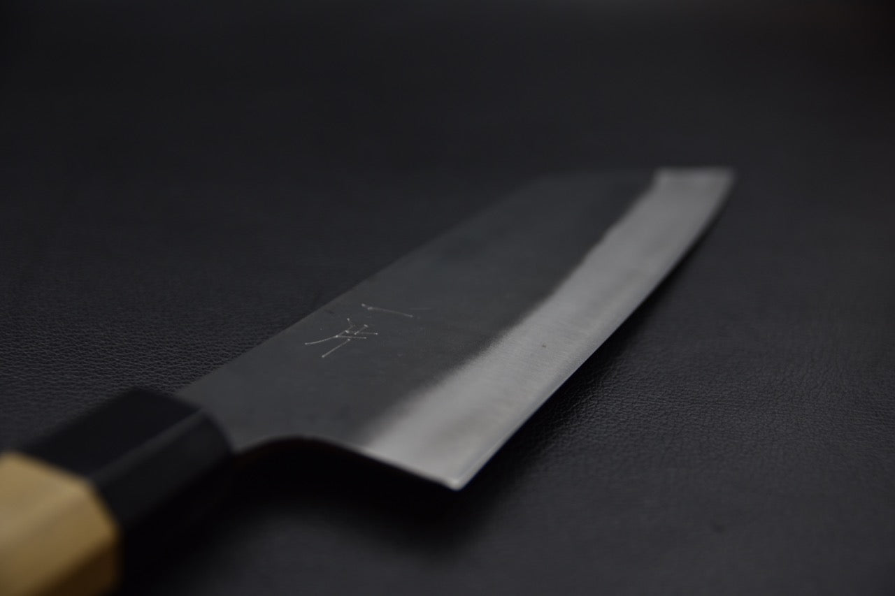 Détail de la lame du couteau japonais montrant le biseau poli sur fond sombre.