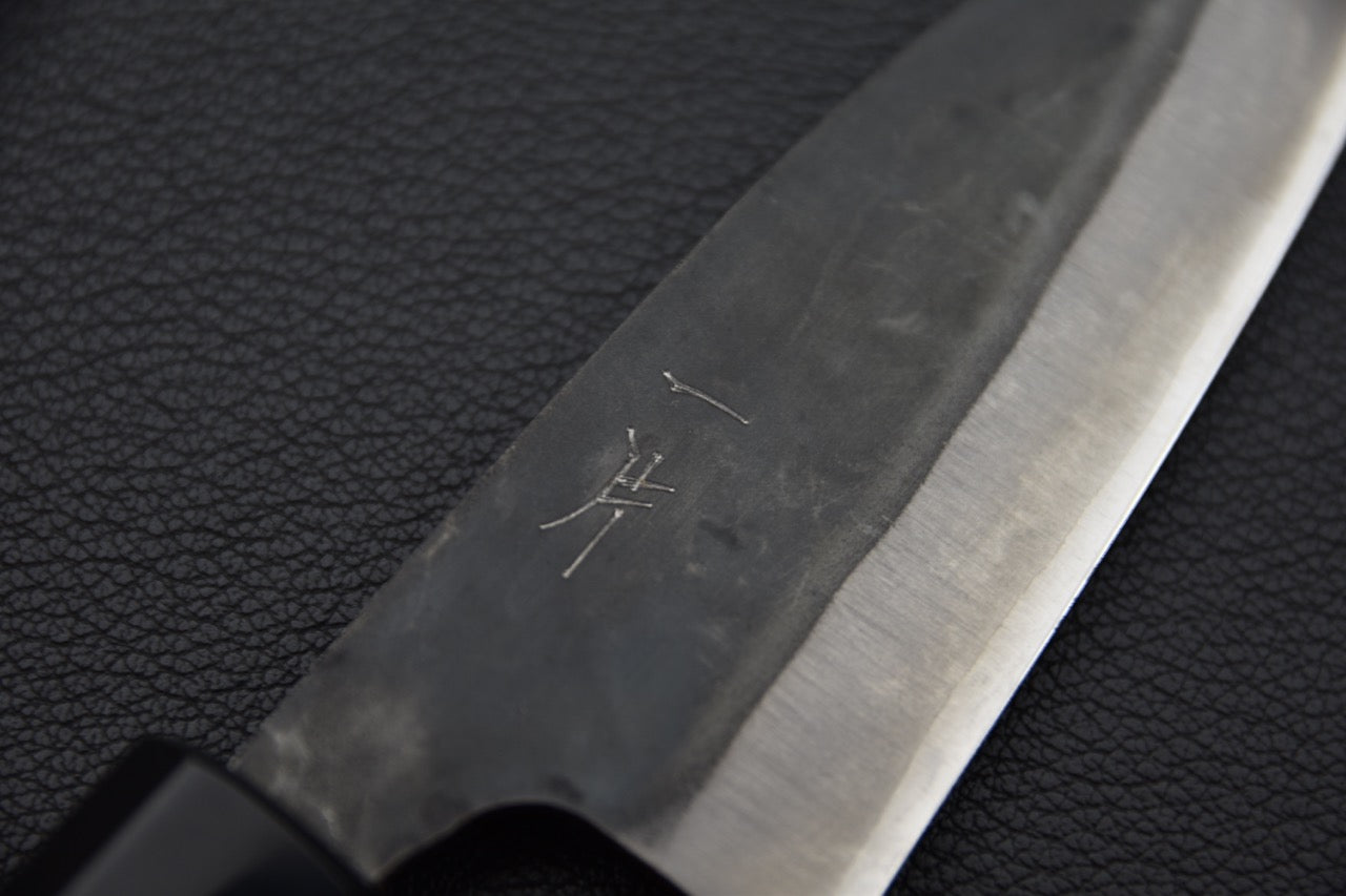 Gravure sur la lame d’un couteau japonais en acier carbone avec kanji visibles.