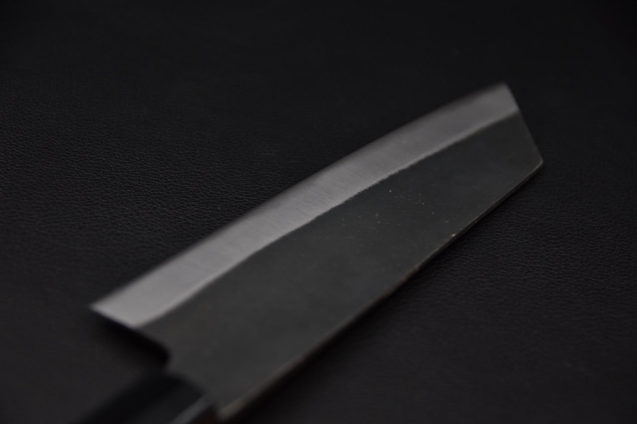 Détail de la lame d’un couteau japonais bunka Hitohira Hizen, finition kurouchi et biseau poli.