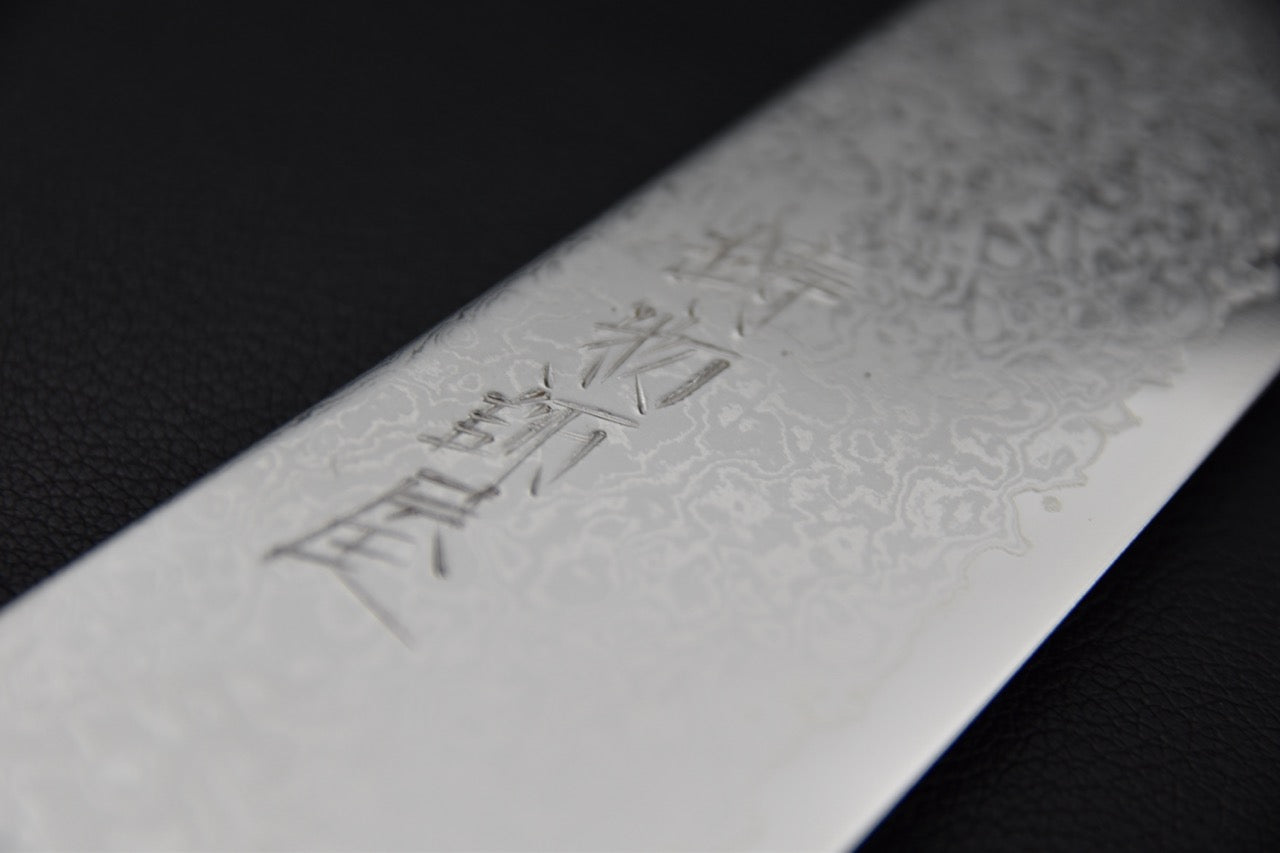 Gros plan sur la gravure japonaise et le motif damassé du couteau japonais Hitohira Imojiya TH Damascus.