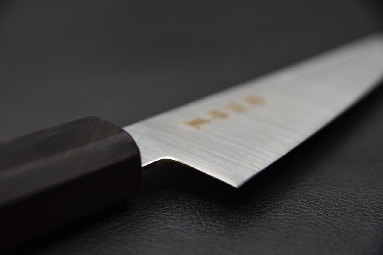 "Vue rapprochée de la jonction entre le manche en ébène et la lame du couteau japonais."