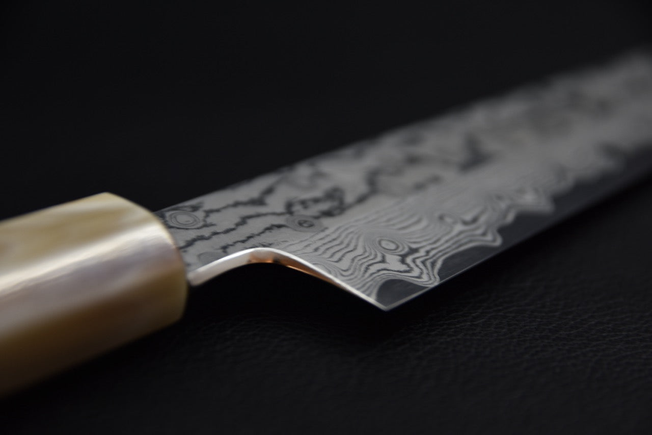 Couteau japonais gyuhiki damassé, détail du talon de lame et de l’émouture près du manche.