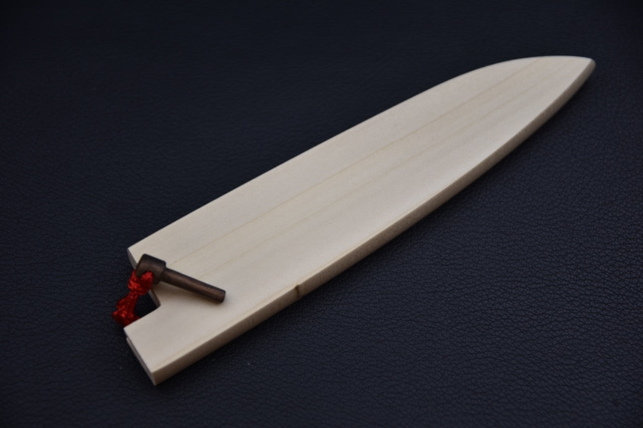 Light wooden saya for a Japanese petty knife, shown on a dark background with its pointed tip and red cord with pin visible.