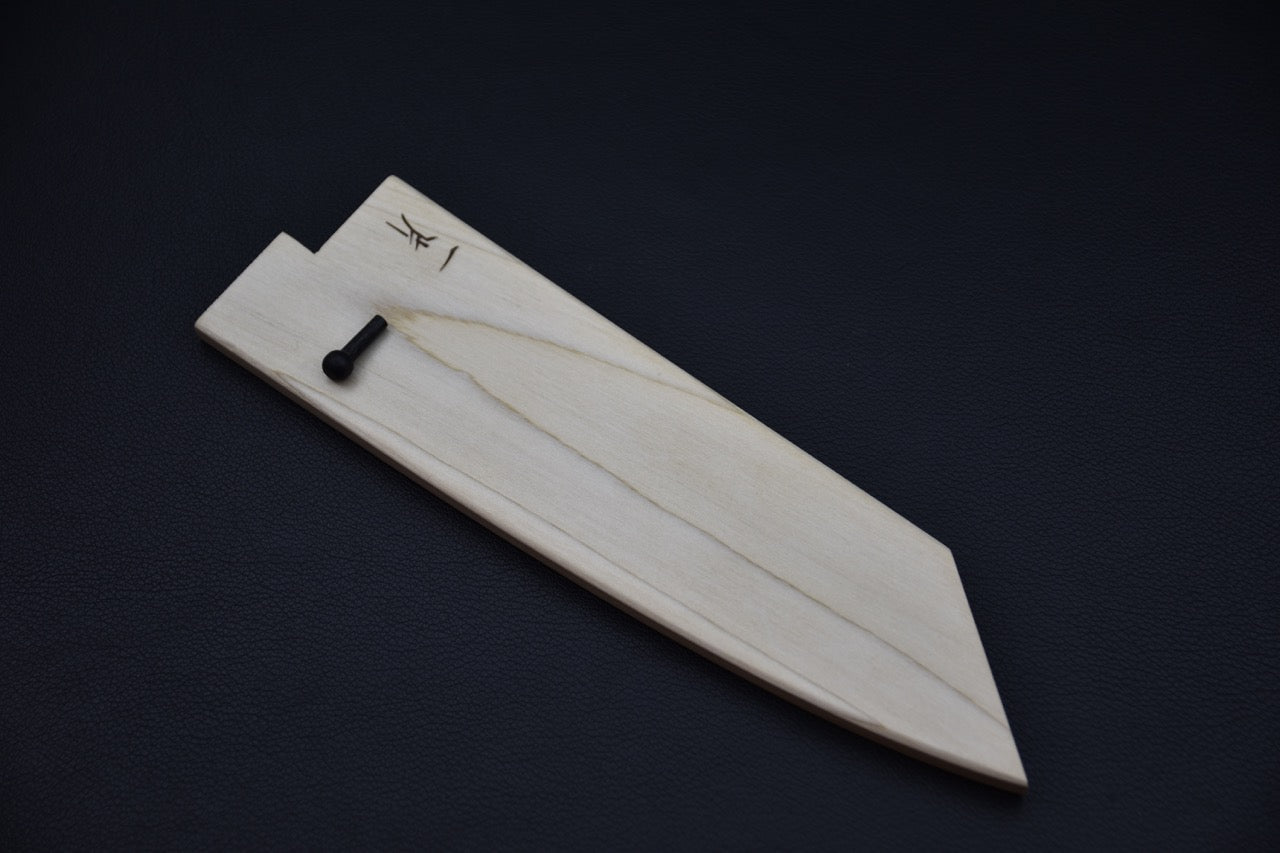 Light wooden saya designed for a Japanese bunka knife, shown on a dark background with its simple shape and smooth finish clearly visible.