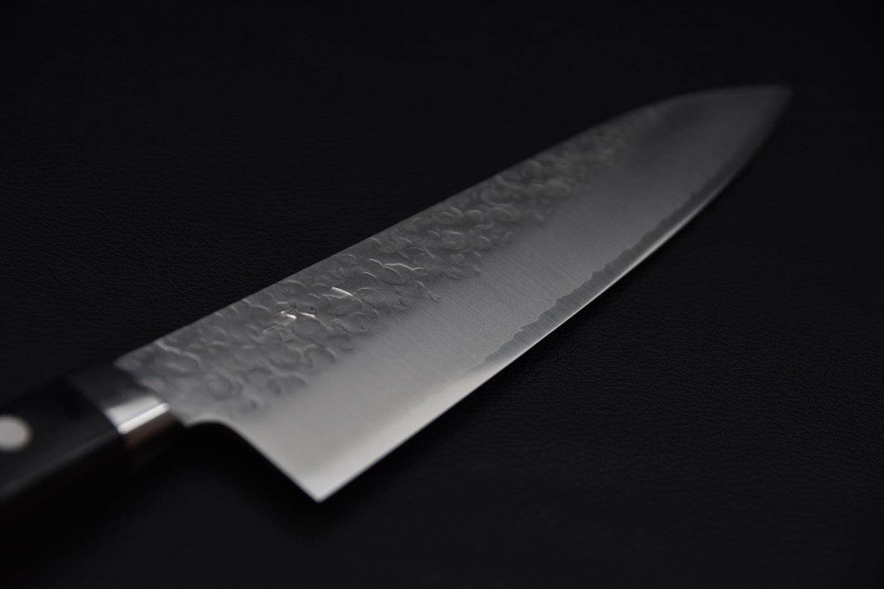 Couteau de chef japonais avec lame martelée et manche noir sur fond sombre