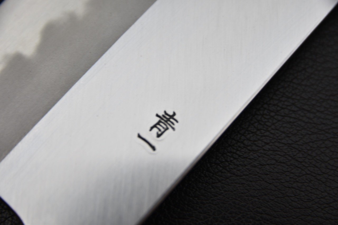 Gros plan sur la lame d'un couteau japonais avec des inscriptions en kanji