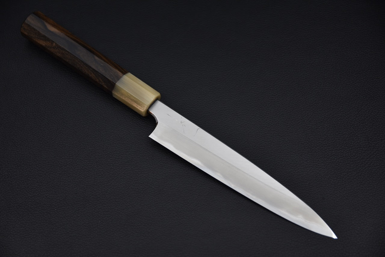 Japanese petty knife with a polished long blade and wa-style wooden handle, displayed on a dark background.
