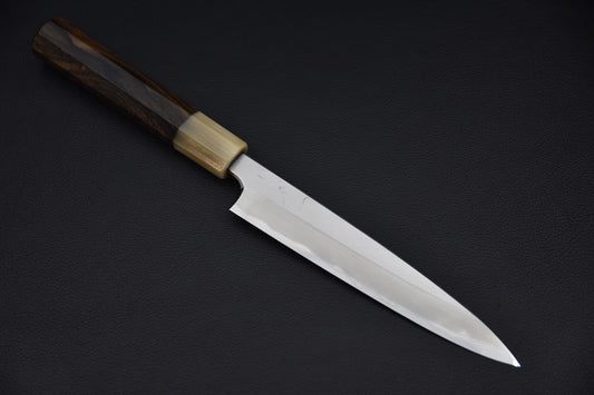 Japanese petty knife with a polished long blade and wa-style wooden handle, displayed on a dark background.