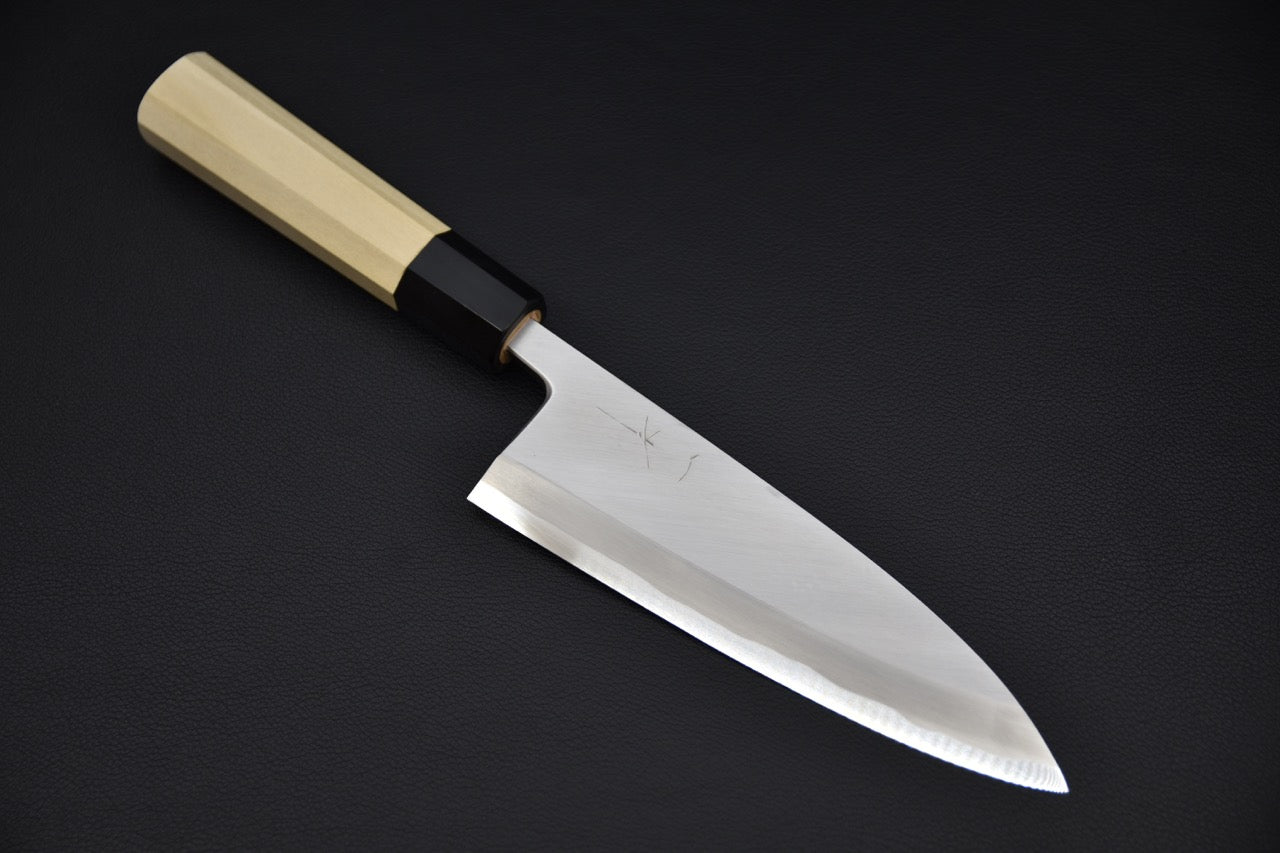 Japanese deba knife with a polished wide blade and light wooden handle, displayed on a dark background.