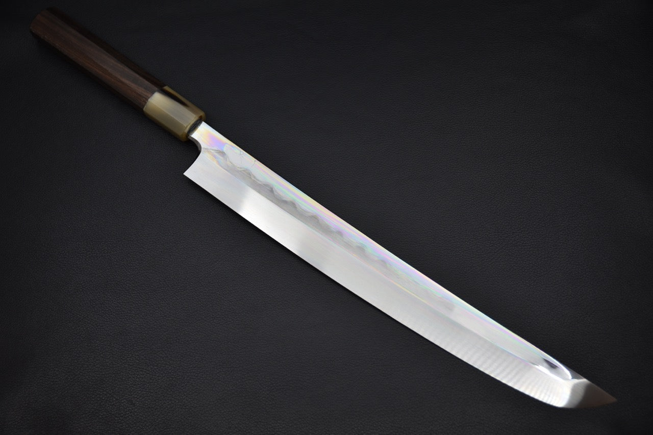 Japanese sakimaru yanagiba knife with a long polished blade and dark wa-style handle, displayed on a dark background.