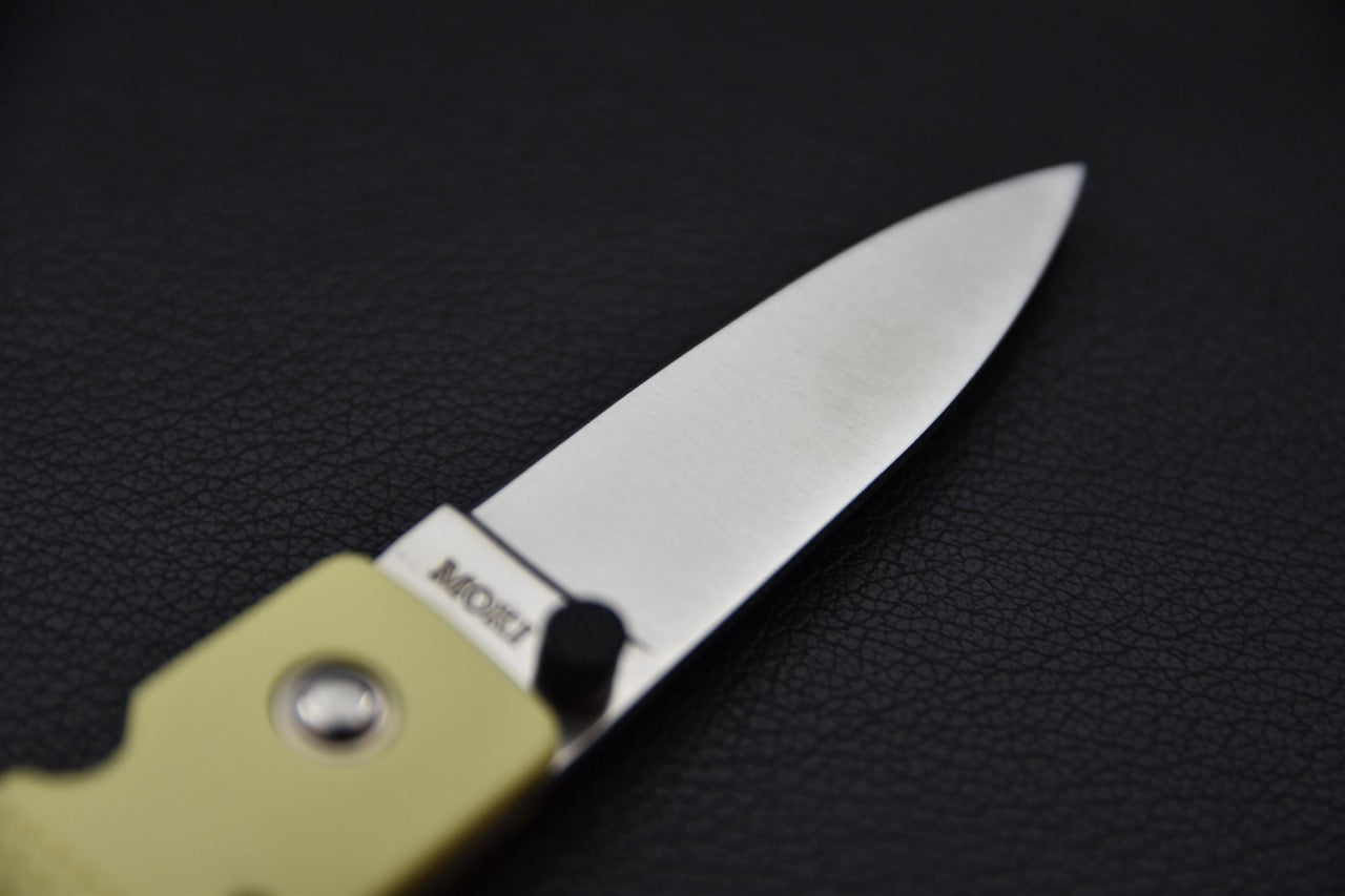 Gros plan sur le marquage MOKI et la lame satinée en acier AUS-8 du couteau pliant japonais