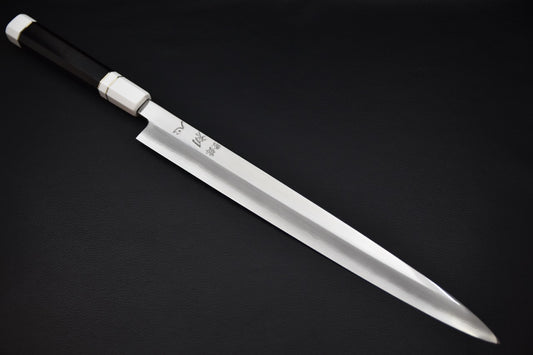 Japanese yanagiba knife with a long polished blade and a dark wooden handle, displayed on a dark background.