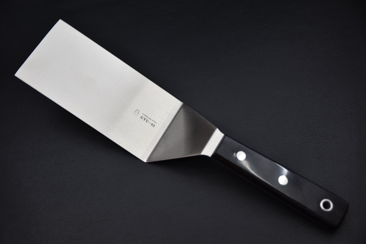   - Spatule japonaise Sekishin GTU-03, détail du manche noir riveté et de l’œillet, accessoire pour couteau japonais — Stay Sharp Montréal.
