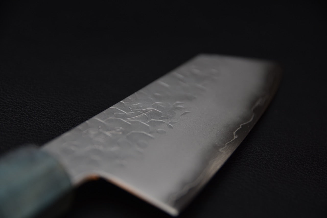 Gros plan sur la lame polie d’un couteau japonais Ko-Bunka avec motifs martelés.