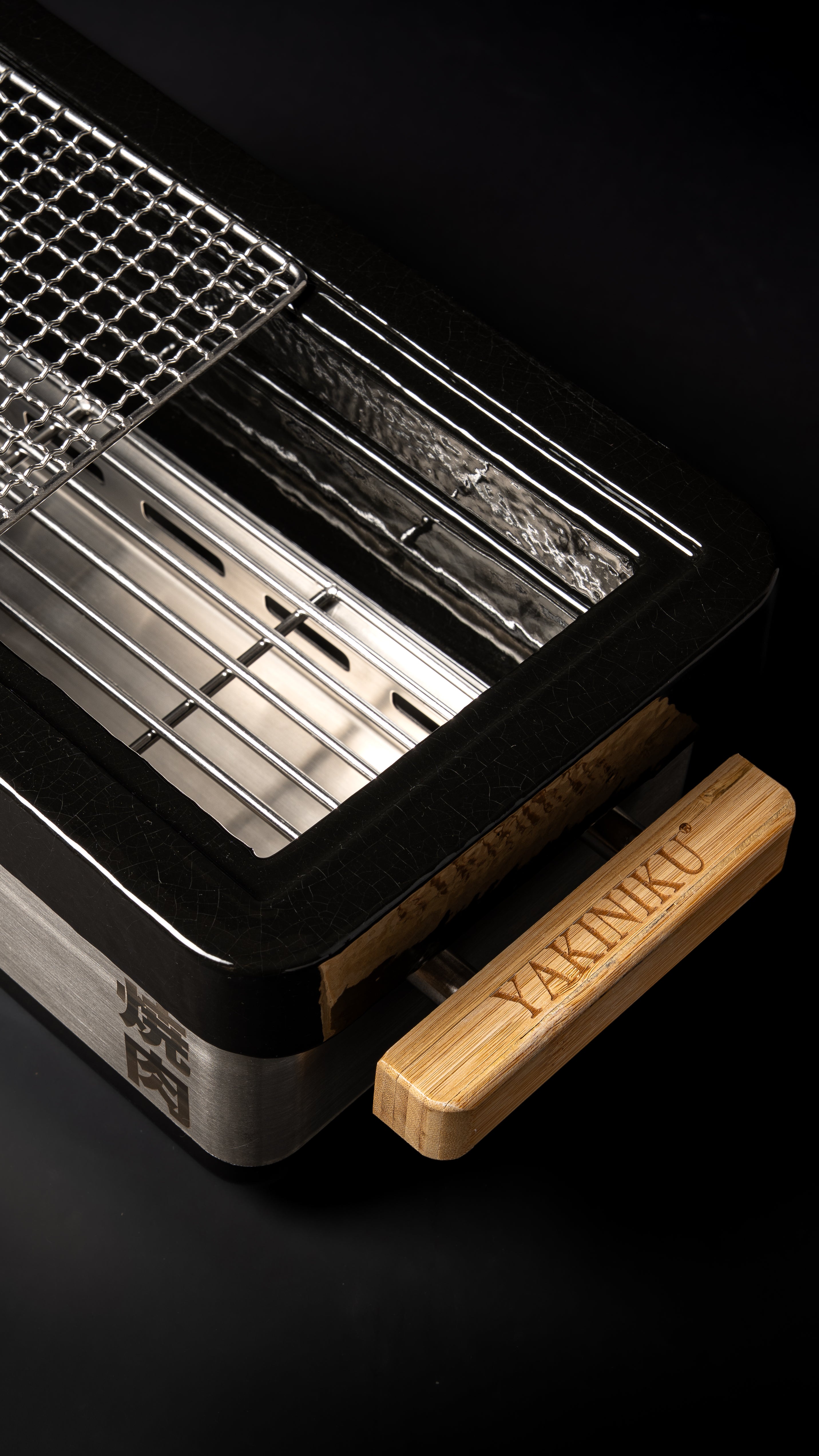 Détail du grill japonais YAKINIKU Shichirin PRO avec poignée en bois gravée et grille de cuisson relevée.