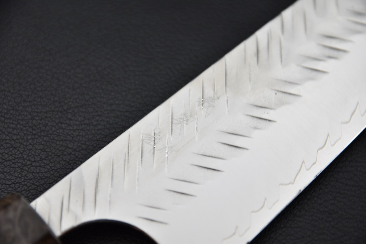 Gros plan sur la lame d’un couteau japonais Kiritsuke Gyuto avec motif strié unique.