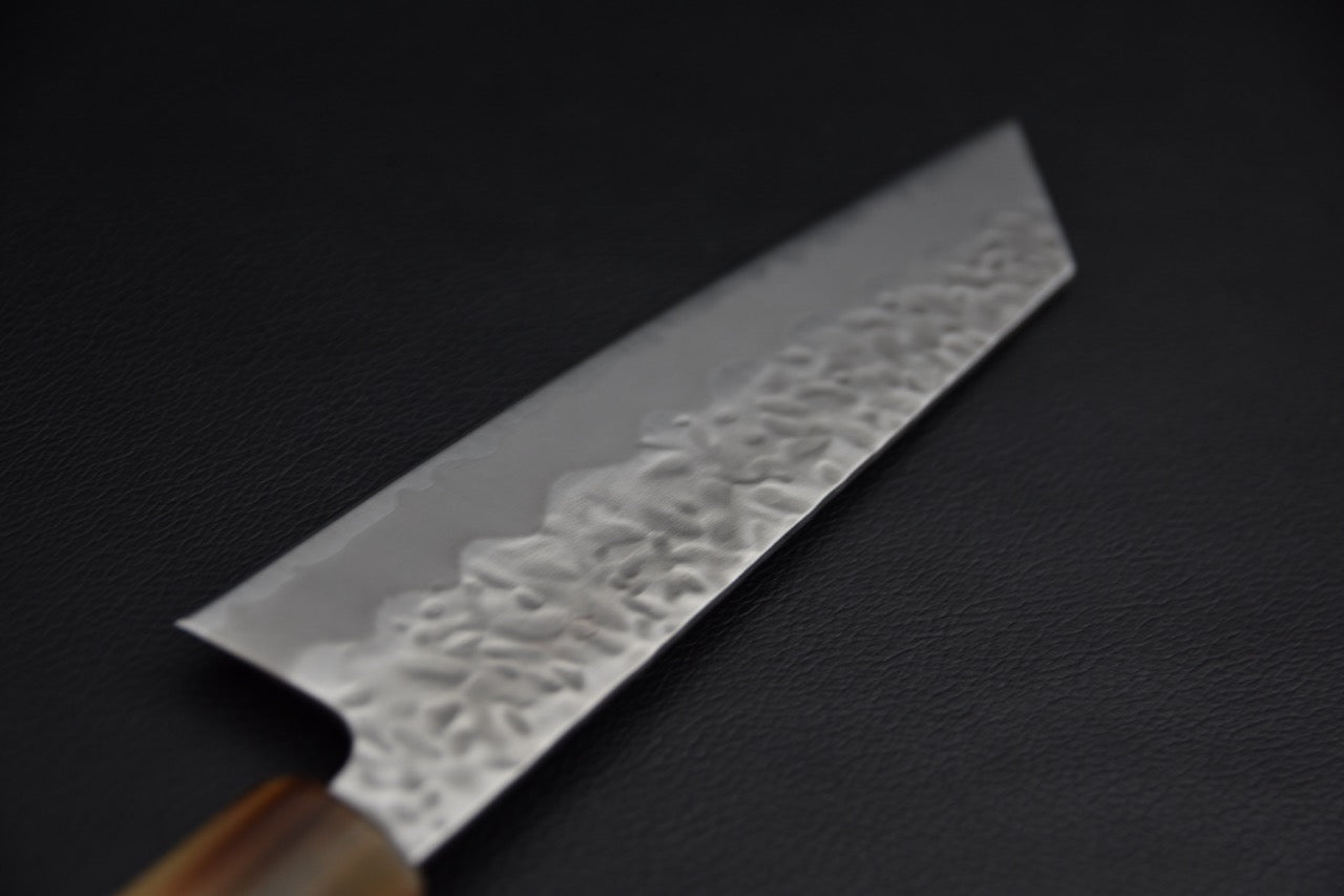 Couteau japonais bunka, gros plan sur la pointe k-tip et la finition tsuchime, fond noir