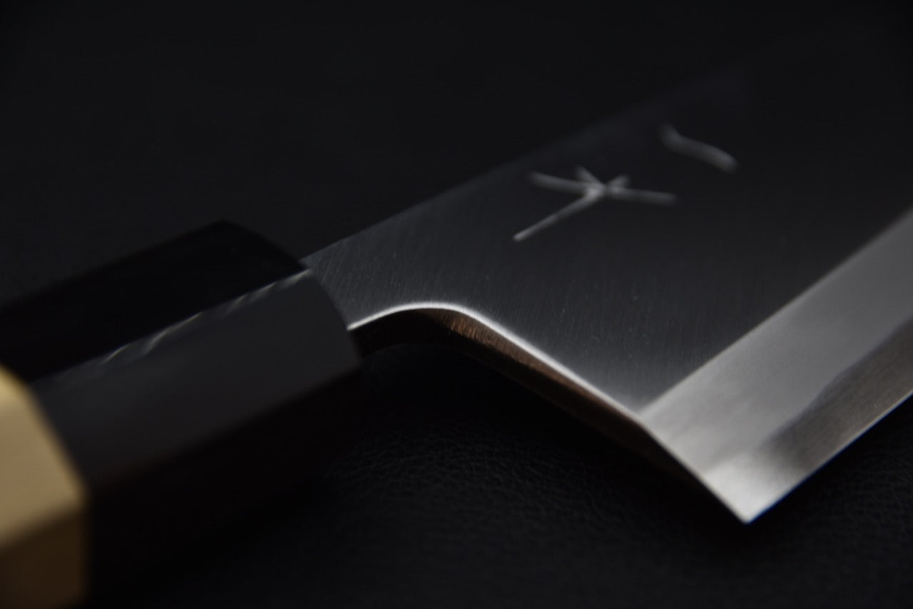 Gros plan sur la lame en acier du couteau Deba Hitohira avec manche en bois élégant