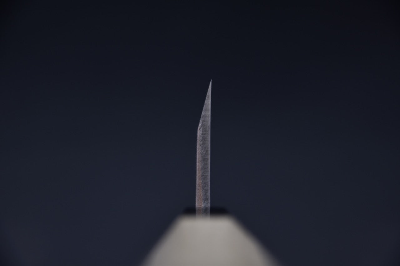 Gros plan sur la lame fine et tranchante d'un couteau Deba japonais sur fond sombre