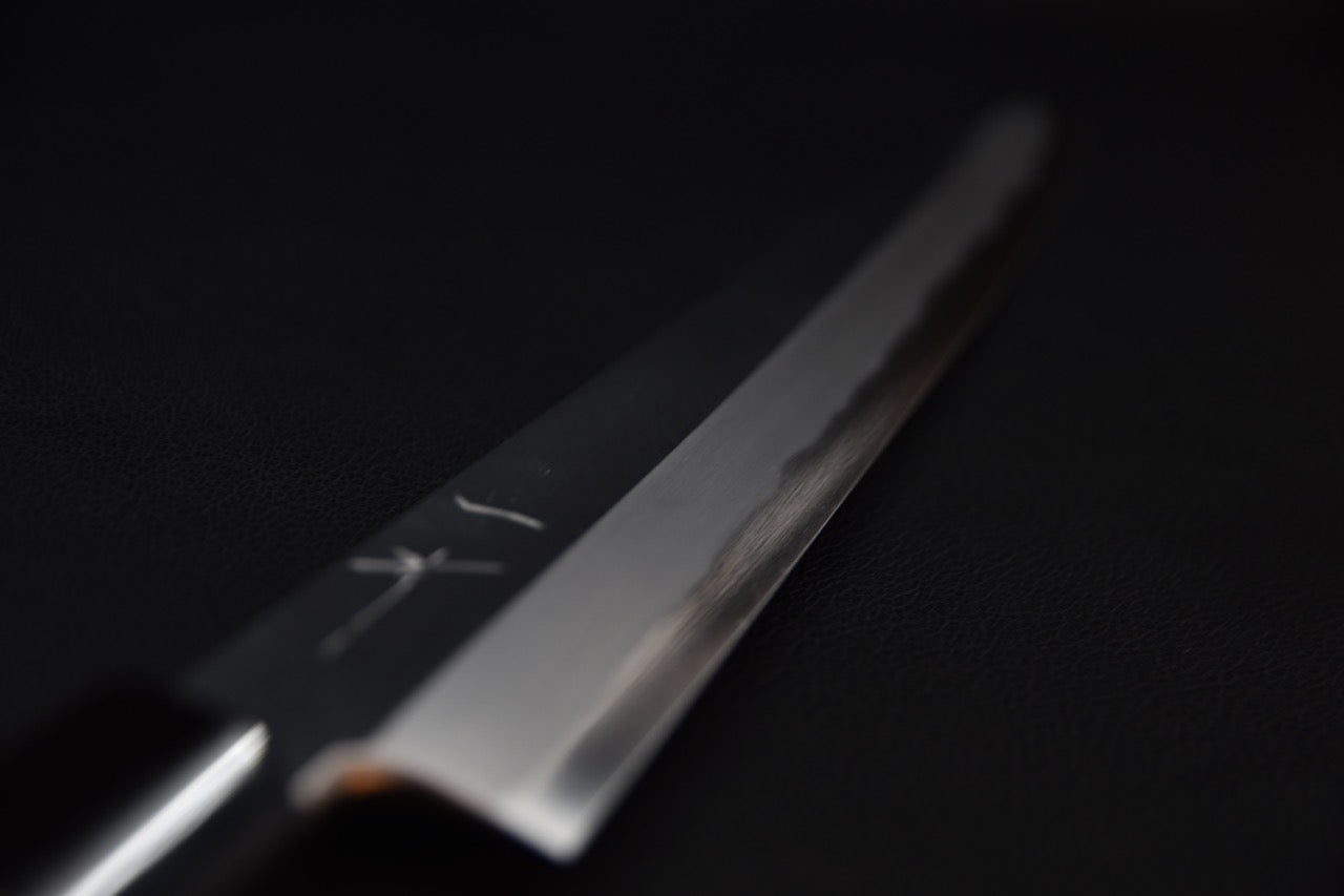 Gros plan sur la pointe d'un couteau japonais Kiritsuke yanagiba sur fond sombre