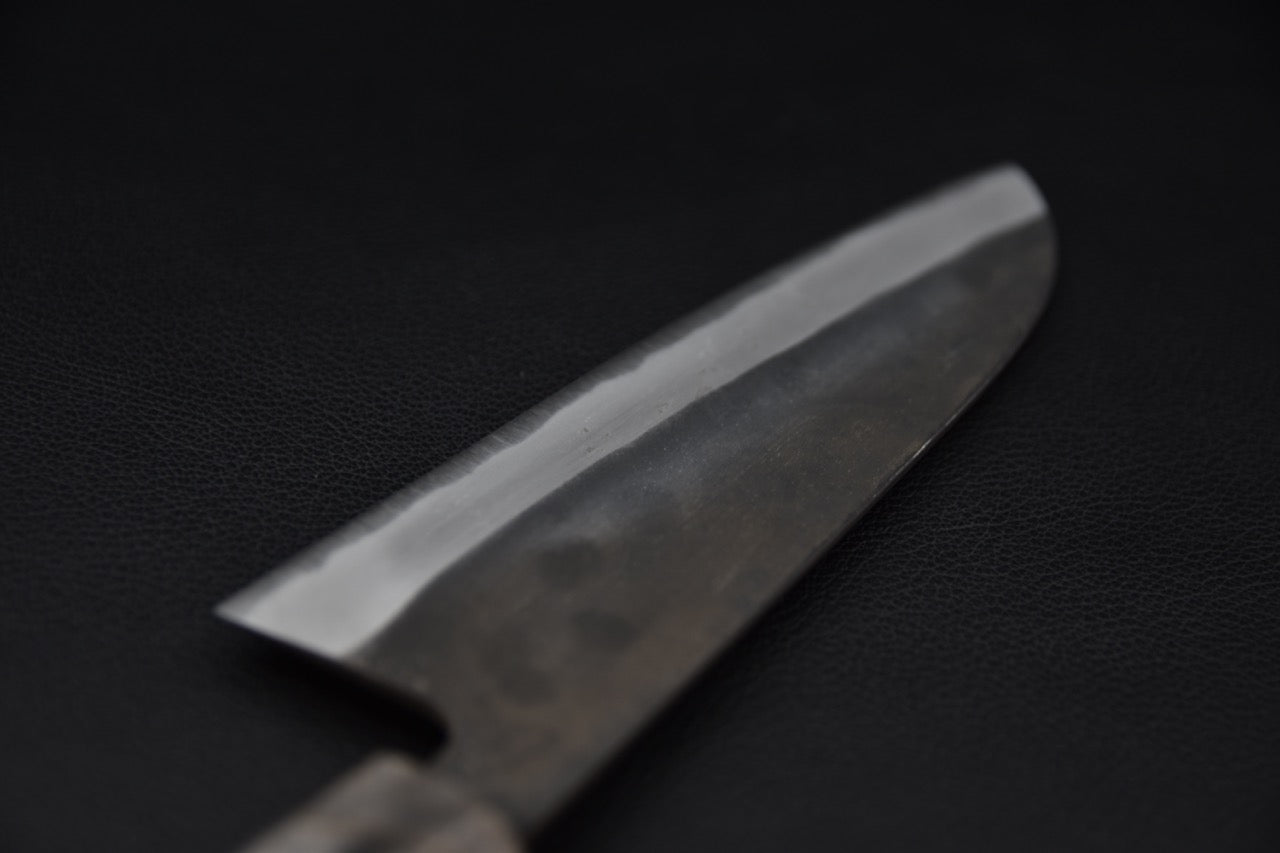 Couteau Santoku en acier Kurouchi sur fond noir mettant en valeur la lame élégante et durable