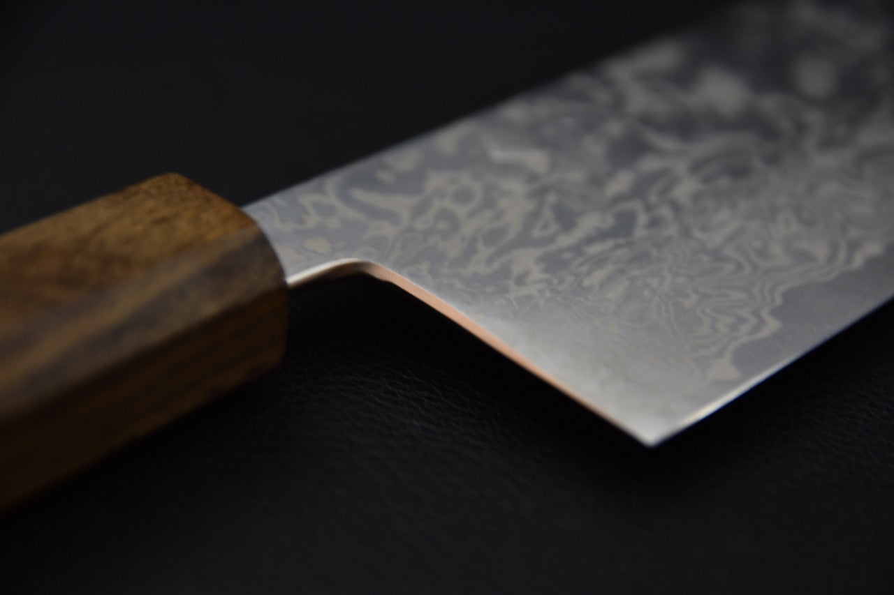 Gros plan sur la lame en acier Damascus du couteau japonais Tsubaki avec motif ondulé distinctif