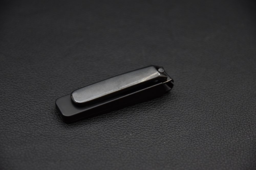 Black metal nail clipper with a sleek minimalist design, displayed on a dark textured surface.