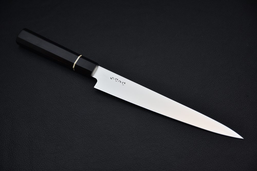 Japanese kitchen knife with a long stainless steel blade, dark wooden handle, and metal ferrule placed on a black textured background.