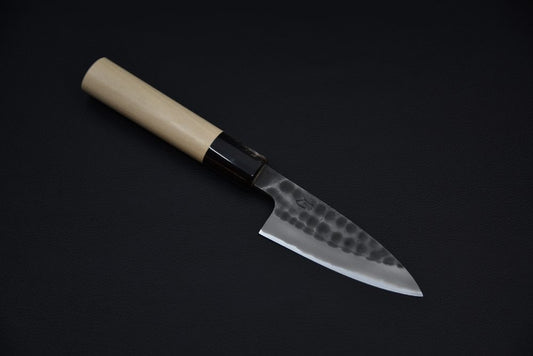 Japanese knife with a hammered tsuchime blade and light wooden handle, displayed on a dark background.