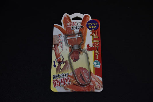 Japanese crab leg peeler in full retail packaging, showing metal blade and illustrated instructions, displayed on a dark background.