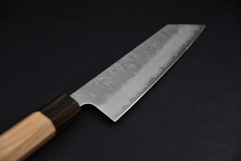 Japanese chef knife with a hammered stainless steel blade and a two-tone wooden handle on a black textured background.