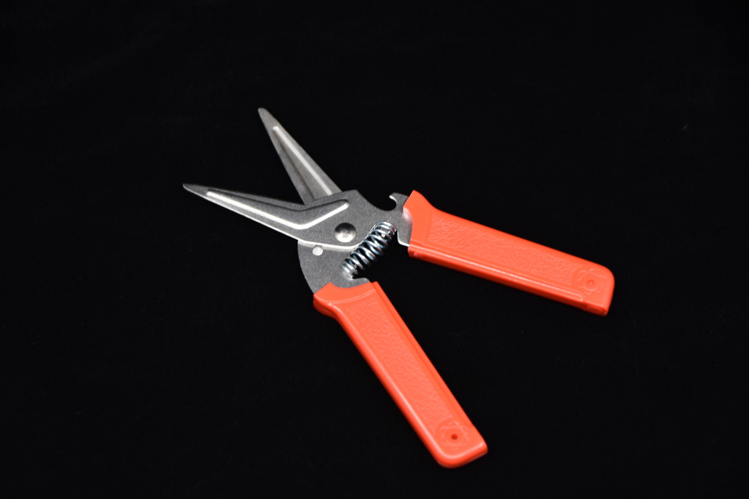 Stainless steel kitchen shears with bright orange handles and a spring-loaded design, displayed on a dark background.