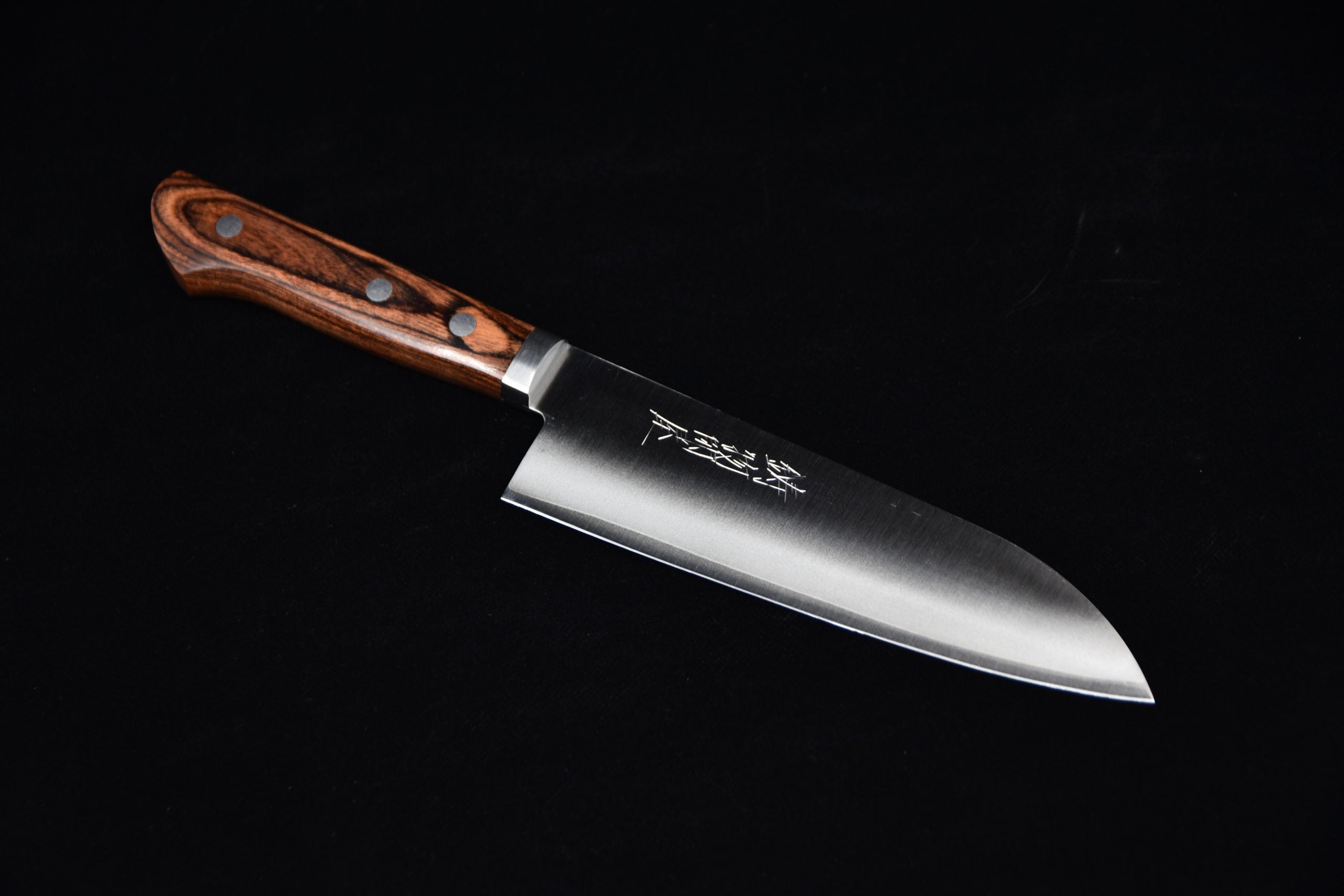 Japanese santoku knife with a wide stainless steel blade and a brown wooden handle featuring three rivets, placed on a black background.
