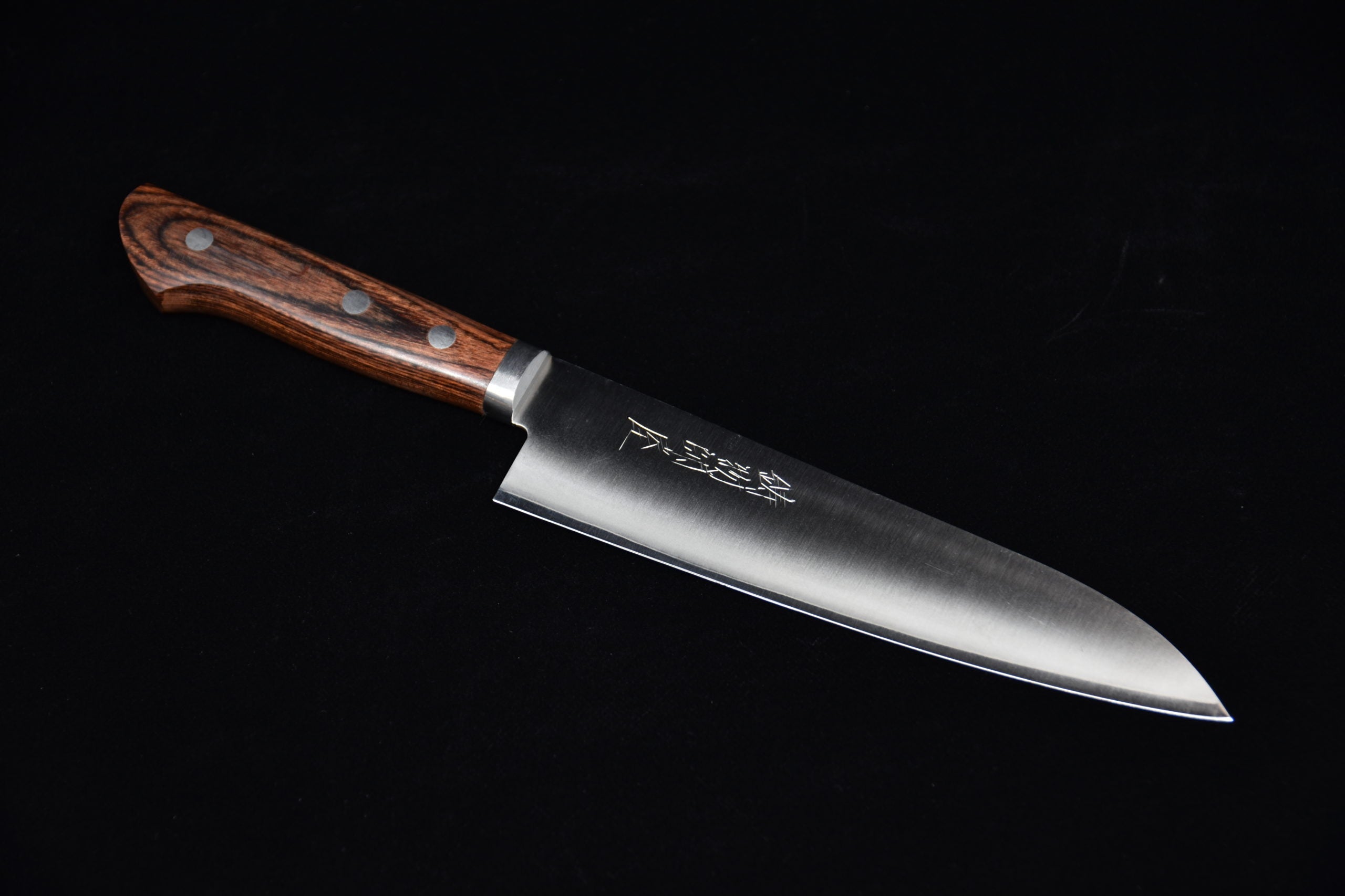 Japanese chef knife with a stainless steel blade and a brown wooden handle featuring three rivets, displayed on a black background.