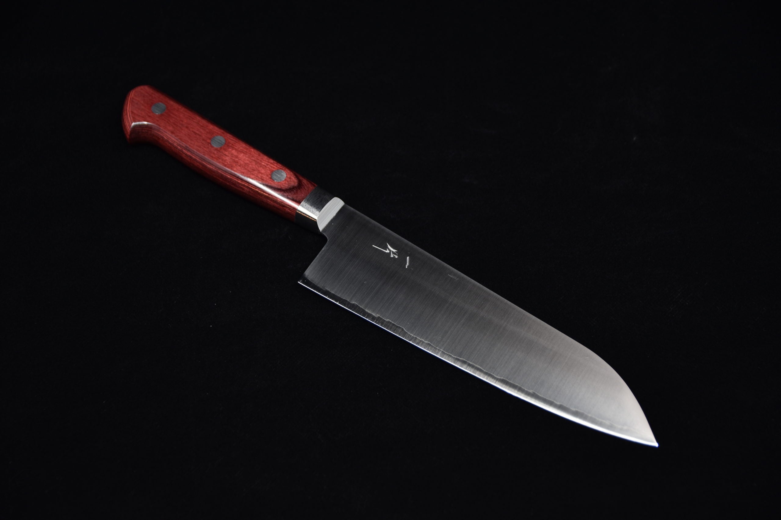 Japanese santoku knife with a stainless steel blade and a red wooden handle featuring rivets, placed on a black background.
